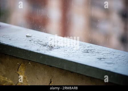 Day shot of raindrops falling from the grey skies and onto the wet surface of a balcony railing, creating ripples in the still water , Belgrade, Serbi Stock Photo