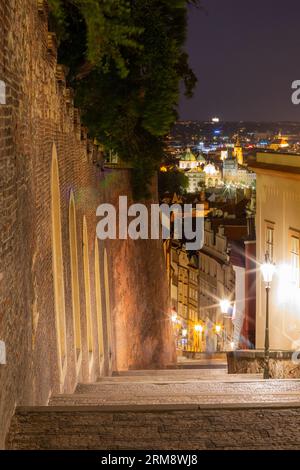 Stunning night time view of illuminated downtown Prague, taken from a quaint cobblestone alleyway on the hilltop next to the walls of Prague Castle Stock Photo