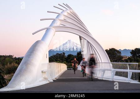 New Plymouth, New Zealand - August 23rd 2017 - Three youths riding their bikes across Te Rewa Rewa Bridge on the Coastal Way with Mt Taranaki Stock Photo