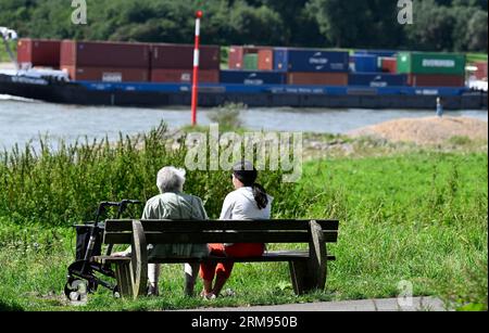 27 August 2023, North Rhine-Westphalia, Hitdorf: Walkers sit on the banks of the Rhine and enjoy the sun. Summer temperatures seem to have come to an end. Despite the sun, the readings only reached values around 20 degrees. Photo: Roberto Pfeil/dpa Stock Photo