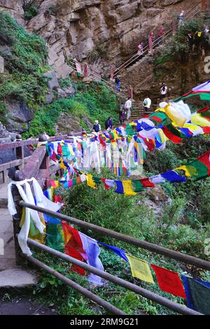Visitors hike past colorful prayer flags as they begin the final ascent up the stairs to the Tiger's Nest Monastery (Taktsang) near Paro, Bhutan Stock Photo