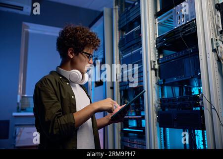 Serious young man working in data center standing at open server rack cabinet Stock Photo