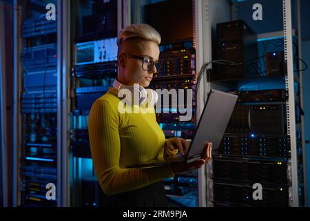 Side view of woman engineer working on laptop at network equipment Stock Photo