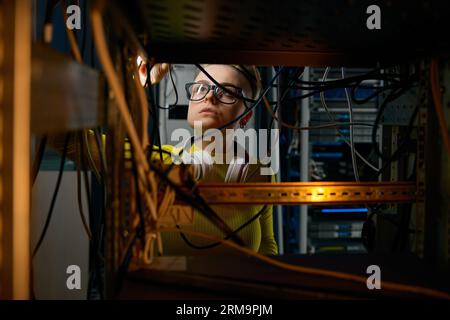 Young woman IT engineer working in datacenter room connecting cables Stock Photo