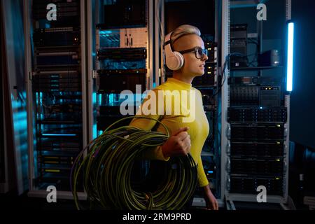 Young woman IT technician walking with wires through server rack in data center Stock Photo