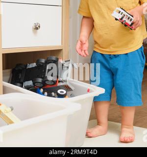 The child is putting the toys back in the box after playing. Kid toddler boy aged two years Stock Photo