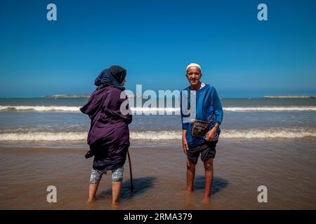 Essaouira, Morocco - August 3, 2023: Elderly couple at the beach wearing traditional clothes. The Muslim religion prevents women from showing their bo Stock Photo