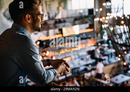 Happy businessman, restaurant owner proudly looking at crowded restaurant Stock Photo