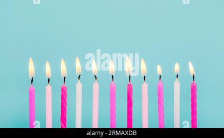 11 pink and white color birthday candles burning in a row isolated on blue. Happy Birthday card design concept.  Bottom lower border edge. Stock Photo
