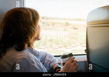 beautiful woman sitting on a train with a cup of coffee looking through the window Stock Photo