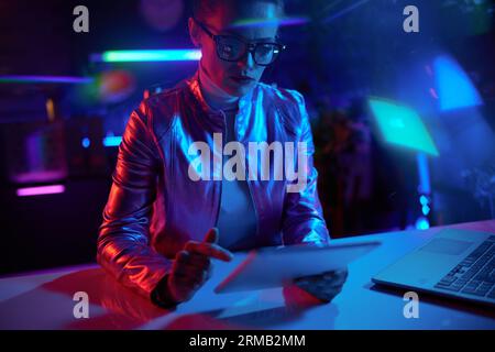 Neon metaverse futuristic concept. elegant business woman in glasses using tablet PC in modern office. Stock Photo