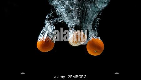 Clementines, citrus reticulata, Fruits falling into Water against black Background Stock Photo