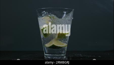 Green Citrus, citrus aurantifolia, falling into a Glass of Water, Stock Photo