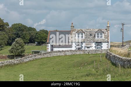 Remote lichen covered scottish cottage surrounded by stone walls against a blue sky Stock Photo