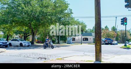 NEW ORLEANS, LA, USA - AUGUST 19, 2023: Man without helmet runs a red light on his motor scooter at an intersection during rush hour Stock Photo