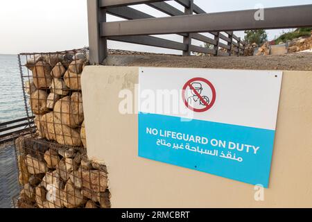 No lifeguard on duty sign, Dead Sea steps and beachside. Bilingual sign warning cautious swimming Stock Photo