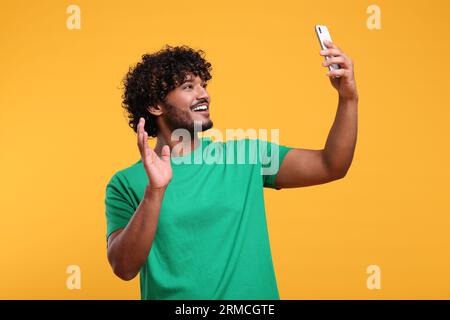 Handsome smiling man having video call via smartphone on yellow background Stock Photo