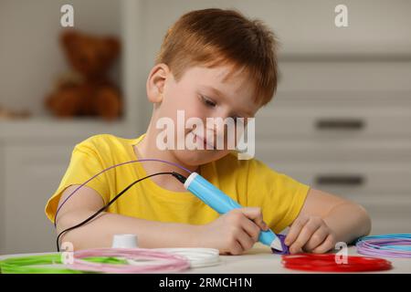 Boy drawing with stylish 3D pen at white table Stock Photo