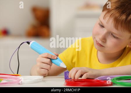 Boy drawing with stylish 3D pen at white table Stock Photo