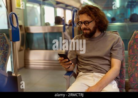 Young smiling man use smartphone while traveling in public transport  Stock Photo