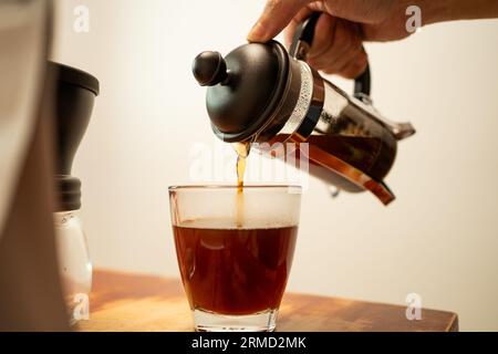 Pouring hot coffee from a french press jug into a drinking glass Stock Photo