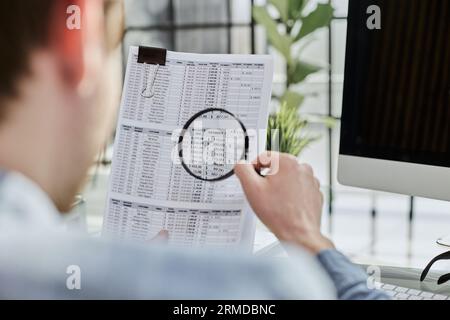 man looking through a magnifying glass to documents notebook. Stock Photo