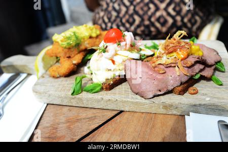 A selection of Smørrebrød served on a wooden cutting board. Copenhagen, Denmark. Stock Photo