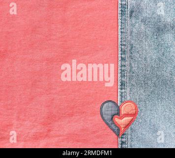 Pink and light blue denim background with a seam and felt heart. Coral and blue colors denim jeans fabric texture with heart-shaped textile patch. Val Stock Photo