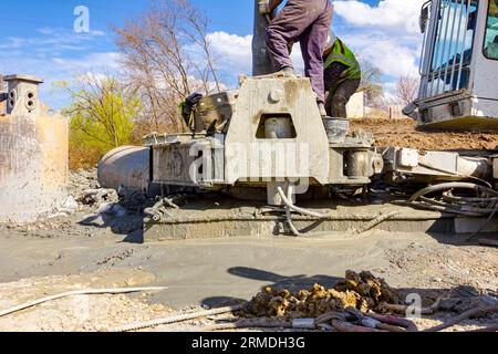 Workers are using shovels to control and directs, fresh concrete into bridge foundation, under construction on river coast. Stock Photo