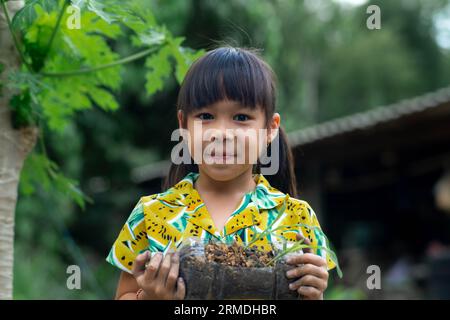 Little girl shows saplings grown in recycled plastic bottles. Recycle water bottle pot, gardening activities for children. Recycling of plastic waste Stock Photo