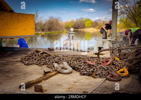View on pile of used chain with hooks and steel cable for lifting of burden with crane. Bridge foundation is under construction on river coast. Stock Photo