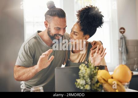 Interracial couple, video call and happy with laptop, wave hello and smile in kitchen, home and web chat. Excited man, young woman and contact with Stock Photo