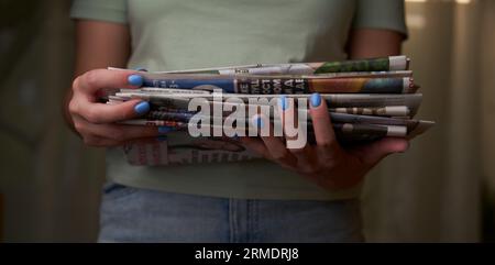 A woman stacks old newspapers in a pile, waste paper collect. Preparing paper waste for recycling. Stock Photo