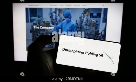 Person holding cellphone with logo of German pharmaceutical company Dermapharm AG on screen in front of business webpage. Focus on phone display. Stock Photo