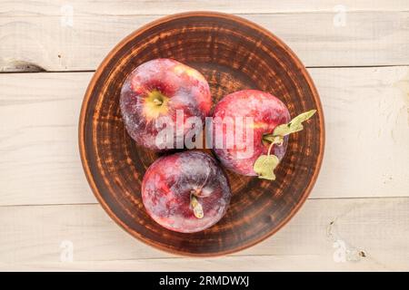 Three ripe juicy red apples with clay plate on wooden table, macro, top view. Stock Photo