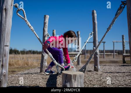 A little girl climbs onto a balance beam in an outdoor obstacle course Stock Photo