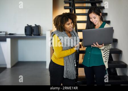 Smiling businesswoman showing laptop computer to female colleague while standing on steps in office Stock Photo