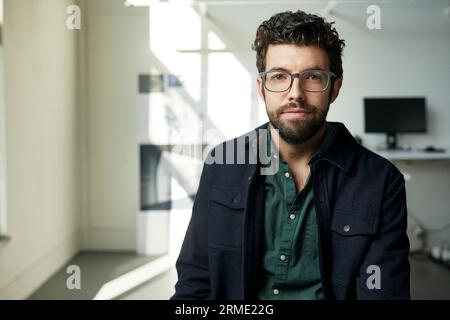 Portrait of confident bearded businessman sitting against wall in office Stock Photo
