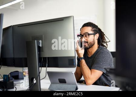 businessman talking over smart phone while sitting at desk in office Stock Photo