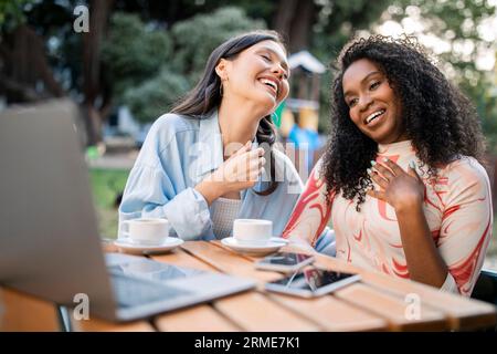 Two Happy Laughing Young Women Using Laptop In Cafe Outdoors Stock Photo