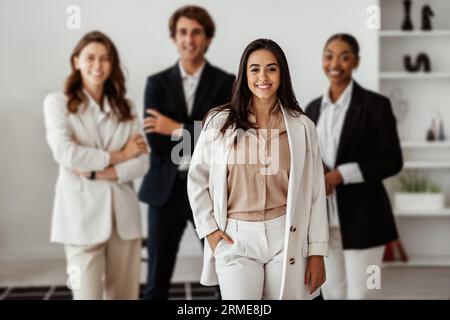 Latin businesswoman leader posing in office interior with her multiracial business team and smiling at camera Stock Photo