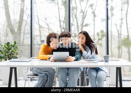 Three multiracial university students using digital tablet searching information for common project, sitting in audience Stock Photo