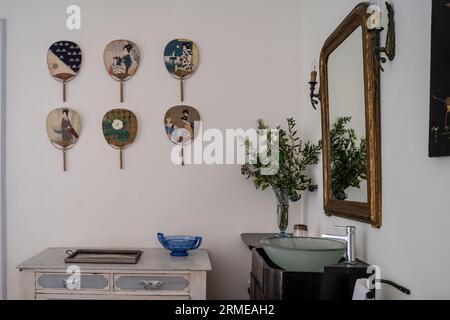 Japanese fans wall-mounted with gilt framed mirror and wash basin Cotignac bedroom, Var, France. Stock Photo