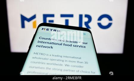 Mobile phone with website of German wholesale company Metro AG on screen in front of business logo. Focus on top-left of phone display. Stock Photo