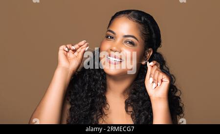 Beautiful latin chubby woman holding dental floss, cleaning teeth with thread, standing over brown background, panorama Stock Photo