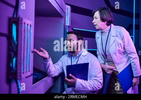 Hindu Male and Adult Female Scientists Engage with Computer in Neon-Lit Science Center Stock Photo