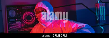 indian scientist in hazmat suit, goggles and medical mask looking away in science center, banner Stock Photo