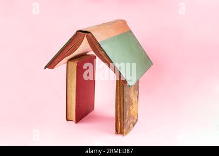 three vintage books arranged in the shape of a house on pink background Stock Photo