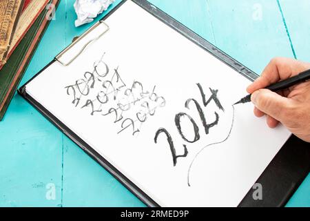 hand with pen writing past and present years number, 2024 new year resolution on a clipboard Stock Photo