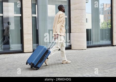 Rear view of young African American businessman in formalwear pulling suitcase with baggage while hurrying to airport or train station Stock Photo